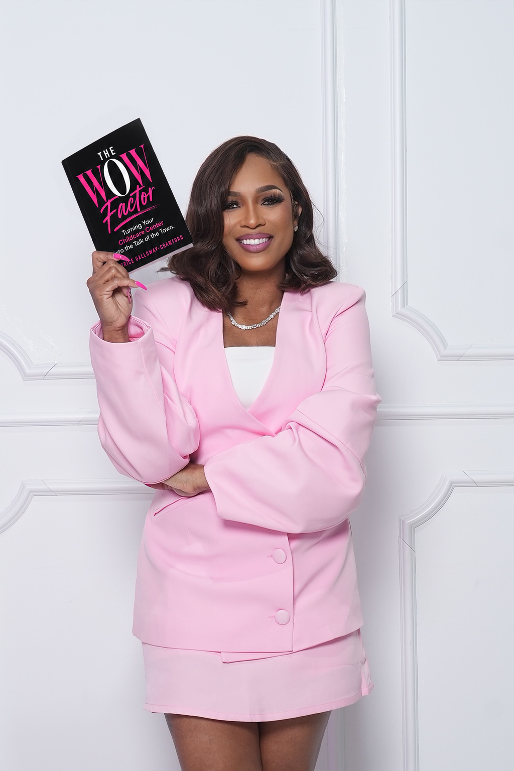 Author in a pink suit holding up a copy of The WOW Factor by Latrice Galloway-Crawford